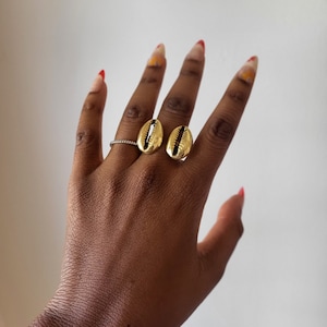 May include: Two gold shell-shaped rings on a hand with red nail polish.