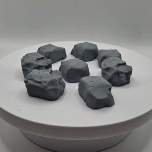 May include: Eight grey, textured, irregularly shaped rocks. The rocks are made of a smooth, hard material and have a slightly rough surface.