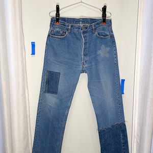 May include: Blue denim jeans with patches and a frayed hem. The jeans have a classic straight leg style.