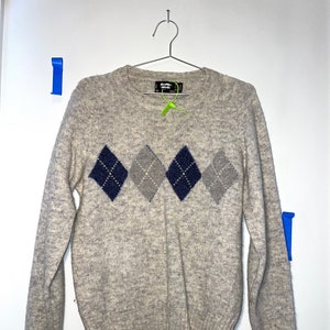 May include: A light gray sweater with a diamond pattern in shades of gray and blue. The sweater has a crew neck and long sleeves.