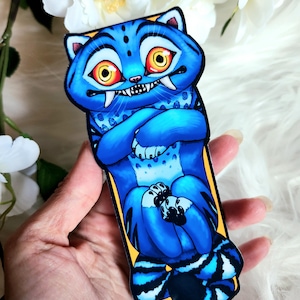 May include: A blue cat-like creature with orange eyes and sharp teeth. The cartoon character has its arms crossed and is set against a yellow border. The design features a spotted pattern and a striped tail. The image is a sticker or a similar product.