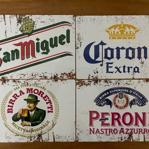 May include: Four vintage metal signs featuring different beer brands. The top left sign is white with red and green text that reads "San Miguel". The top right sign is white with blue text that reads "Corona Extra". The bottom left sign is white with a brown and white illustration of a man holding a beer glass and the text "Birra Moretti Una Storia Italiana". The bottom right sign is white with red text that reads "Peroni Nastro Azzurro Birra Superiore D'Italia Dal 1846".