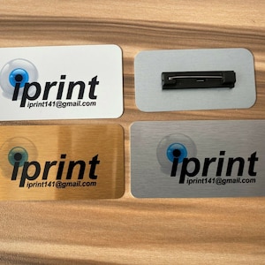 May include: Four different name tag designs featuring a blue eye logo and the text "iprint iprint141@gmail.com". One design is white, one is gold, one is silver, and one is a blank silver name tag with a black pin.