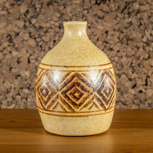 May include: A ceramic vase with a light brown glaze and a geometric pattern in brown. The vase has a rounded body and a narrow neck.