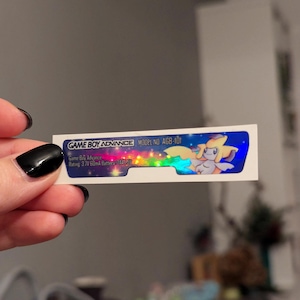 May include: A holographic sticker for a Game Boy Advance with the text "GAME BOY ADVANCE MODEL NO AGB-101" and "Game Boy Advance Rating: 3.7V 60mA Battery 244051". The sticker features a cartoon image of a light blue and yellow Pokemon with a star on its head.