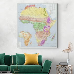 May include: A framed map of Africa, with a detailed geographical representation. The map uses various colours, including green, yellow, and purple, to denote different regions and terrains. The map is displayed on a white wall above a green sofa, with a yellow cushion.