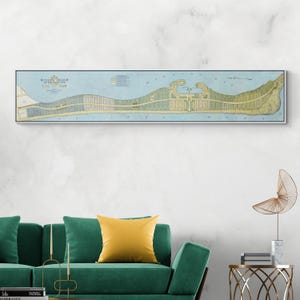 May include: A framed vintage map print of Mission Beach, California, in a long, rectangular format. The map features a detailed illustration of the area with blue, green, and beige tones, and is set against a white wall above a green sofa.