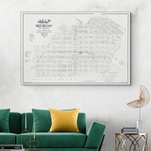 May include: A framed map of Red Bluff, California, with detailed street layouts and text. The map is in black and white, with the title "Map of the Town of Red Bluff" at the top. The map is displayed above a green sofa with a yellow pillow.