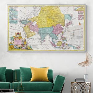 Puede incluir: Un mapa antiguo enmarcado de Asia, con una representación cartográfica detallada en colores pastel. El mapa incluye texto e ilustraciones, mostrando información geográfica histórica. El marco es blanco y el mapa se muestra sobre un sofá verde.