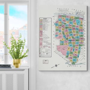 Puede incluir: Una impresión de mapa vintage con una ilustración detallada y colorida de un plano de la ciudad. El mapa presenta varios bloques de colores, una clave y texto que incluye "Volume Twelve" y "19". La impresión está montada sobre un lienzo blanco.