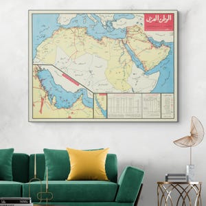 Può includere: Una mappa vintage incorniciata del Medio Oriente e del Nord Africa, con uno sfondo color crema, mari blu e masse terrestri gialle. Linee rosse indicano i percorsi e c'è testo in arabo. La mappa è sopra un divano verde.
