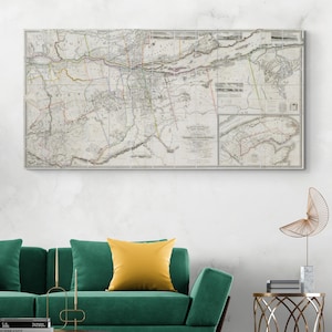 May include: A framed vintage map with intricate cartography, showing a complex arrangement of lines and geographical details. The map is mainly in grayscale with hints of colour. It's displayed above a green sofa with a yellow cushion.