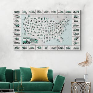 May include: A canvas print featuring a vintage map of the United States, illustrated with various types of trucks. The map is in a light blue color, with the trucks in green and black. The print is displayed on a white wall above a green sofa.
