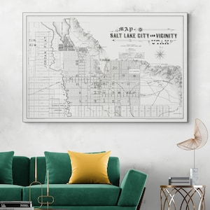 May include: A framed vintage map of Salt Lake City and Vicinity, Utah, in grayscale. The map includes detailed street layouts, geographical features, and text that reads "Map of Salt Lake City and Vicinity Utah."