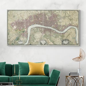 May include: A framed vintage map of London, divided into four panels. The map features a detailed depiction of the city with a river running through it, rendered in muted tones of beige, pink, and green. The map is mounted on a white wall above a green sofa.