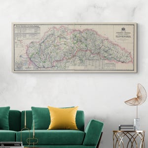 May include: Vintage map of Slovakia, printed on canvas, with a cream background and detailed lines showing roads and railways. The map is framed and hanging on a white wall above a green sofa with a yellow pillow.