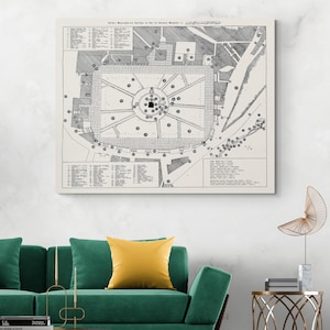 May include: A black and white architectural blueprint of a building, mounted on a white canvas. The blueprint features detailed line drawings of the building's layout, with text and symbols. The canvas is displayed above a green couch with a yellow pillow.