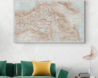 May include: A vintage map of Armenia, printed on paper with a light blue background and brown lines. The map is framed and hanging on a white wall above a green sofa with a yellow pillow.