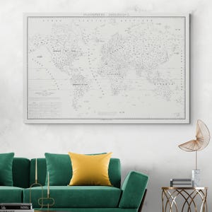 May include: A framed, vintage-style world map titled "PLANISPHERE ZOOLOGIQUE" in black and white. The map is detailed with continents, oceans, and various labels. The frame is white, and the map is displayed on a white wall above a green sofa with yellow pillows.