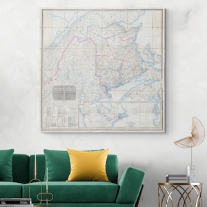 Könnte beinhalten: Eine gerahmte Vintage-Karte von Nova Scotia, Kanada, mit einem Raster. Die Karte zeigt rosa und blaue Linien, die Regionen und Wasserwege hervorheben. Der Titel "NEW BRUNSWICK" ist sichtbar. Die Karte wird über einem grünen Sofa mit einem gelben Kissen angezeigt.