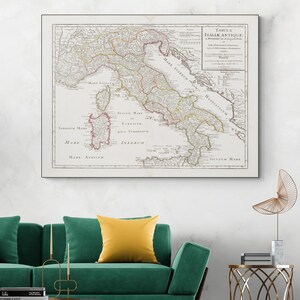 Op de afbeelding: Een antieke kaart van Italië, ingelijst en weergegeven op een witte muur. De kaart, getiteld "Tabula Italiae Antiquae", toont gedetailleerde cartografie met verschillende regio's en wateren, beschreven in het Latijn. De kaart is beige met rode, gele en groene accenten.