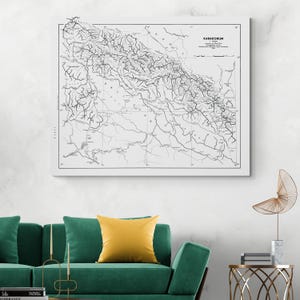 Puede incluir: Un mapa en blanco y negro enmarcado de la cordillera del Karakórum. El mapa presenta intrincadas líneas que detallan el terreno y las vías fluviales. La obra de arte se exhibe sobre un sofá verde con un cojín amarillo.