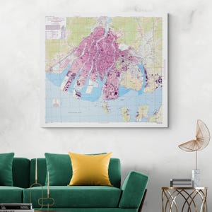 Puede incluir: Una impresión enmarcada de un mapa antiguo que presenta un plano detallado de la ciudad en tonos rosa y verde, sobre un fondo de agua azul. El mapa está montado en un marco blanco, adecuado para la decoración de paredes. El mapa muestra el diseño de la ciudad, incluidas calles y vías fluviales.