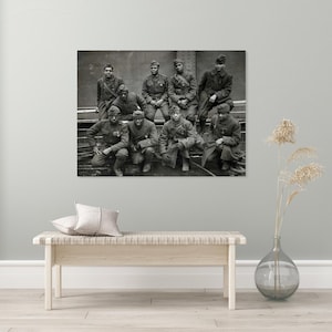 May include: A black and white photograph of a group of soldiers in uniform. The soldiers are wearing hats and coats, and some are kneeling. The photograph appears to be taken outdoors, possibly on a ship or platform.