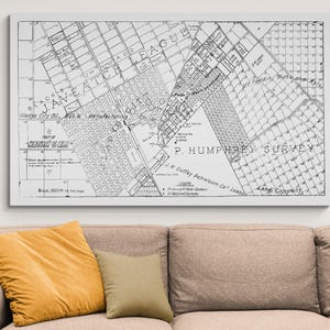May include: A framed black and white map of a city, with text including "JAVEATCH LEAGUE" and "P. HUMPHREY SURVEY". The map is displayed above a beige sofa with yellow and tan pillows.