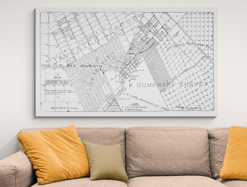 May include: A framed black and white map of a city, with text including "JAVEATCH LEAGUE" and "P. HUMPHREY SURVEY". The map is displayed above a beige sofa with yellow and tan pillows.