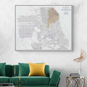 Puede incluir: Un mapa enmarcado de San Francisco de 1906, con una superposición dorada que resalta un área específica. El mapa es en blanco y negro, con detalles de las calles y características geográficas. El marco es negro y el mapa se muestra en una pared blanca.