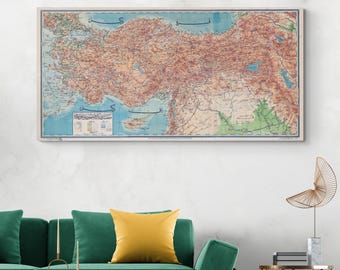 May include: A vintage map of Turkey with Arabic text, printed on a canvas with a light brown frame. The map is displayed on a white wall above a green sofa with yellow throw pillows.