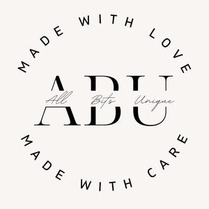 Pu&ograve; includere: Logo in bianco e nero con il testo "ADU" in grassetto. Le lettere sono stilizzate con le parole "All", "Bits" e "Unique" scritte in corsivo all'interno di ogni lettera. Il logo &egrave; circondato da un cerchio con il testo "Made with Love Made with Care" scritto intorno.
