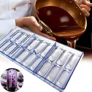 Puede incluir: Un molde de plástico transparente con 15 cavidades rectangulares para hacer barras de chocolate. El molde está sobre una superficie blanca. En el fondo hay una olla de chocolate derretido.