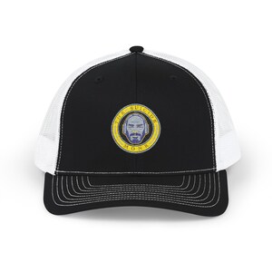 Könnte beinhalten: Schwarz-weiße Trucker-Cap mit gebogenem Schirm. Die Vorderseite ist schwarz, und die Mesh-Rückseite ist weiß. Die Kappe hat einen gestickten Aufnäher mit dem Text "THE SUICIDE MONK" um ein Gesicht.