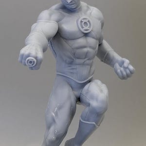 May include: A gray figurine of a superhero in a dynamic pose, with a mask and a chest emblem. The figure is muscular and detailed, with a determined expression. The superhero is wearing a form-fitting suit.