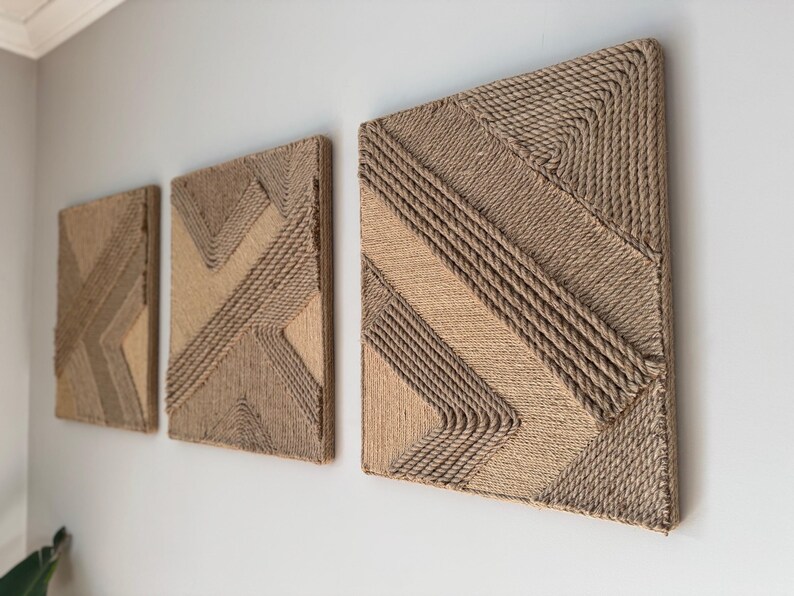 May include: Three rectangular wall art pieces with geometric designs made from natural-colored rope. The artwork is mounted on a light gray wall, showcasing a modern, textured aesthetic. The rope is tightly woven, creating a tactile, dimensional effect.