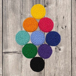 May include: Nine colorful, crocheted coasters arranged on a weathered wooden surface. The coasters are in a variety of colors, including yellow, orange, red, teal, blue, navy, green, purple, and black. Each coaster is round and has a textured appearance.