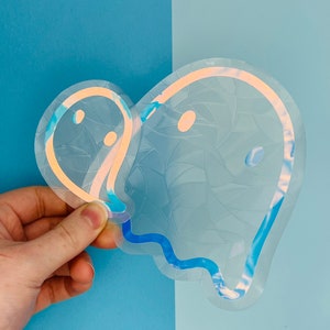 May include: Two iridescent ghost stickers with a blue and orange outline. The stickers are on a blue background.
