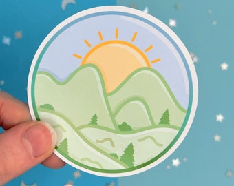 May include: A round sticker with a green mountain landscape and a yellow sun rising over the peaks. The sky is blue and the mountains are green.