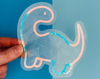 May include: A clear vinyl sticker with a pink and blue marbled design. The sticker is shaped like a dinosaur with a simple outline.
