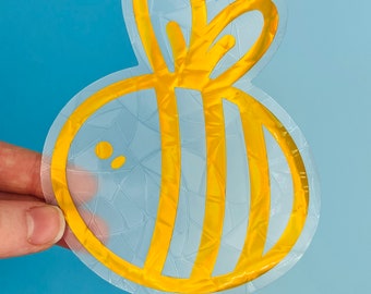 May include: A gold bee sticker with a holographic finish. The bee has a striped body and a heart-shaped head.