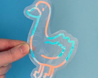 Könnte beinhalten: Ein holografischer Aufkleber mit einem Entenmotiv, der einen blauen und orangenen Umriss hat. Der Aufkleber befindet sich auf einem blauen Hintergrund.