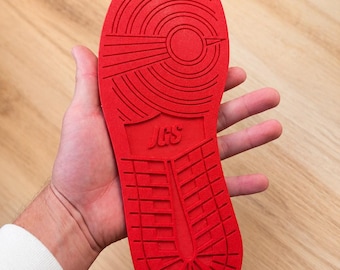 May include: A bright red shoe sole featuring a circular pivot point pattern at the forefoot and a grid pattern at the heel. The center of the sole displays the embossed letters JGS. The tread design consists of concentric circles and lines.