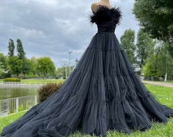 May include: A black strapless tulle gown with a feather trim at the bodice. The gown has multiple layers of tulle and a long train.