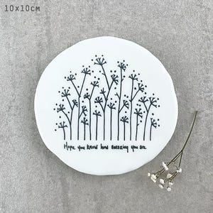 May include: A white ceramic dish with a black floral design and the text "Hope you know how amazing you are." The dish is approximately 4 inches in diameter. A small sprig of white flowers is next to the dish.