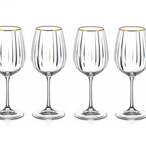 May include: Four clear wine glasses with a gold rim. The glasses have a tall stem and a rounded bowl with vertical lines. The glasses are arranged in a row against a white background.