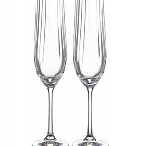 May include: Two clear champagne flutes with a gold rim. The flutes have a tall, slender design with vertical ridges. The stem and base are clear glass. Perfect for celebrations and special occasions.