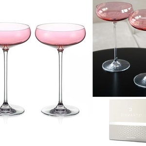 Könnte beinhalten: Set aus zwei rosafarbenen Champagnergläsern mit klarem Stiel und Fuß. Die Gläser sind in einer Schachtel mit dem Diamante-Logo verpackt.