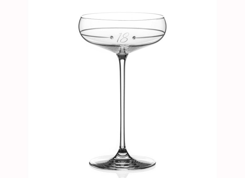 May include: A clear glass champagne flute with a thin stem and a wide bowl. The bowl has a delicate etched design and the number "18" is etched on the side.